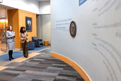 Two women standing in an atrium look at a wall display.
